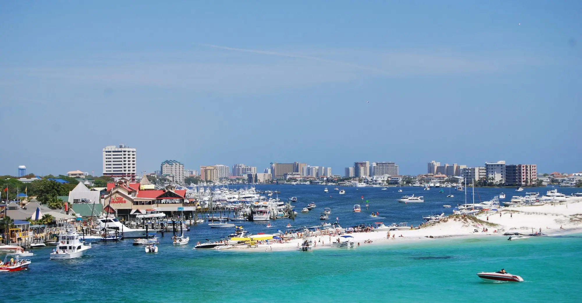 Destin Harbor full of boats with the town and Gulf-front condos behind it and a sandbar in front