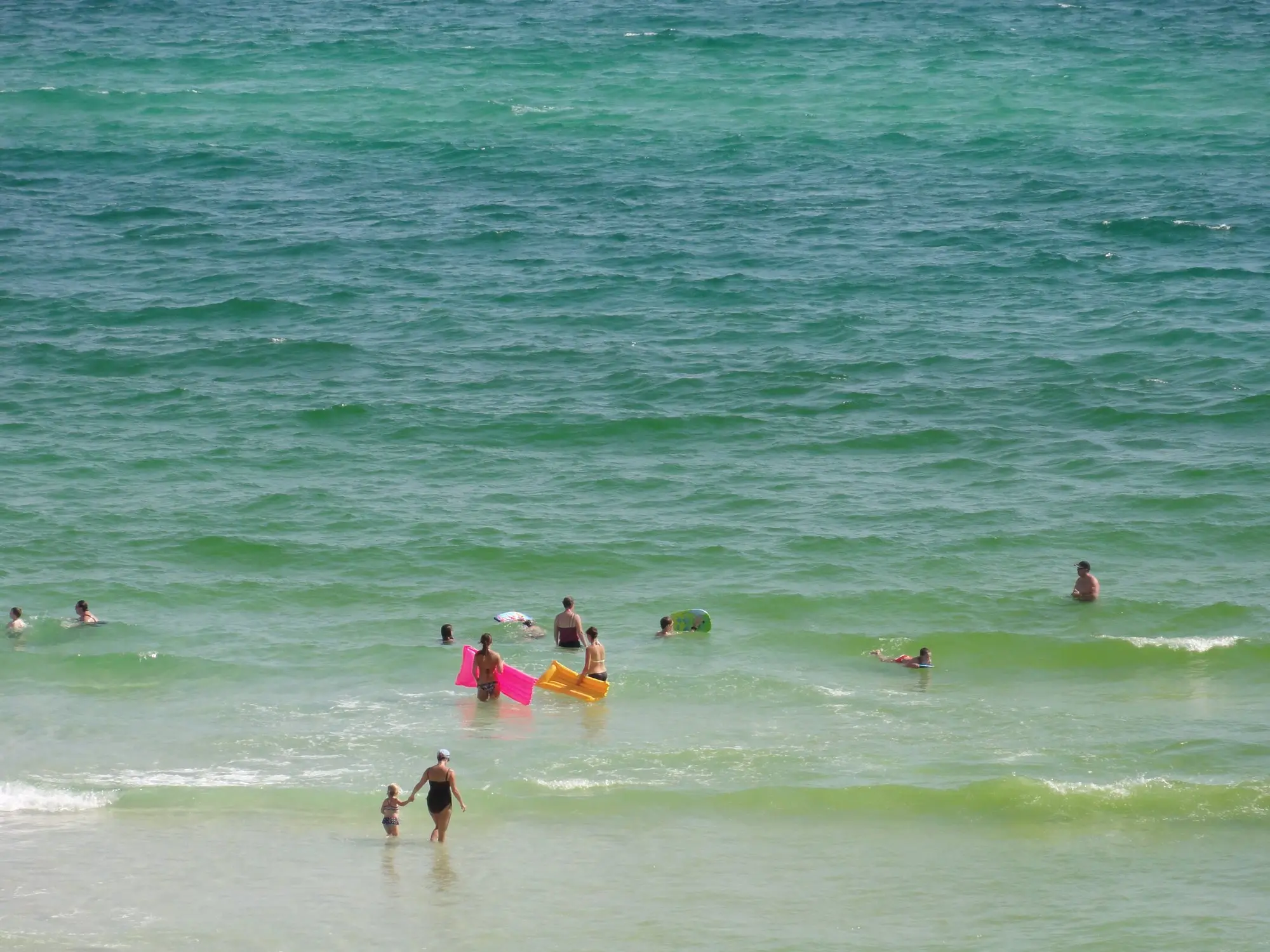 Swimmers in clear green Gulf water off a white-sand beach on Florida's Emerald Coast