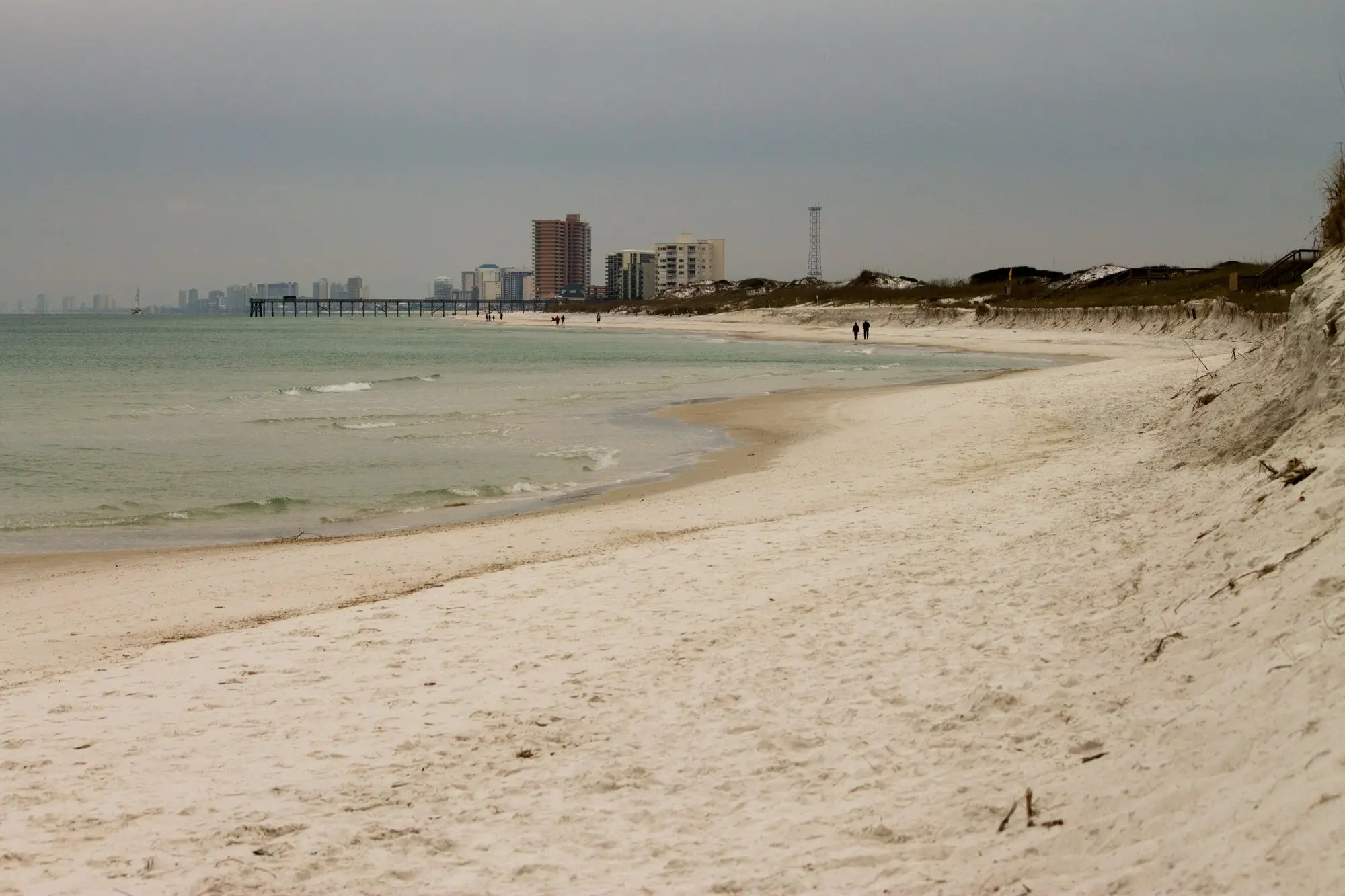 A quiet stretch of Panama City Beach seen from St. Andrews State Park with high-rises and a pier in the distance