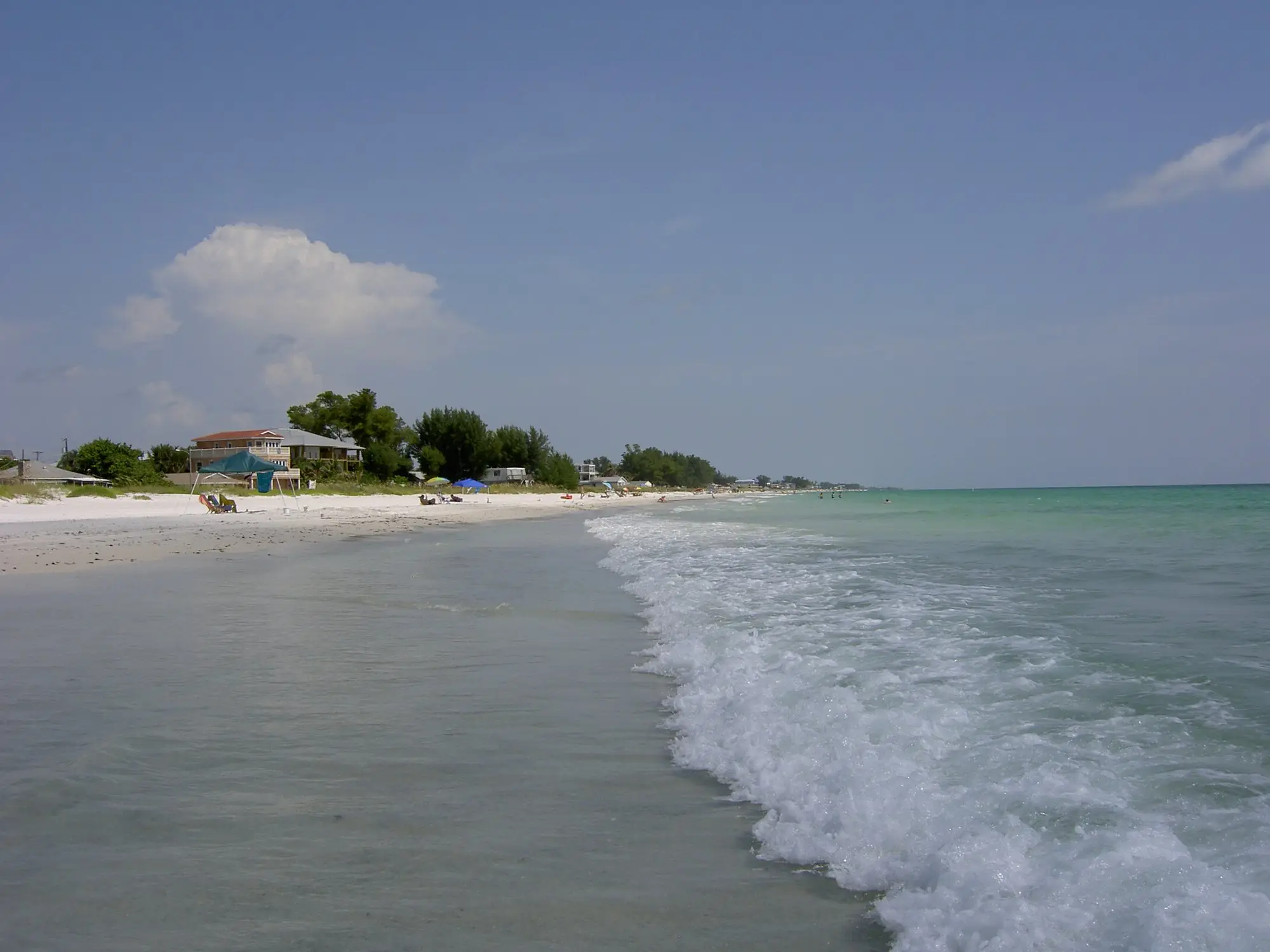 Gentle Gulf surf rolling onto a wide white beach on Anna Maria Island with low beach houses behind the dunes