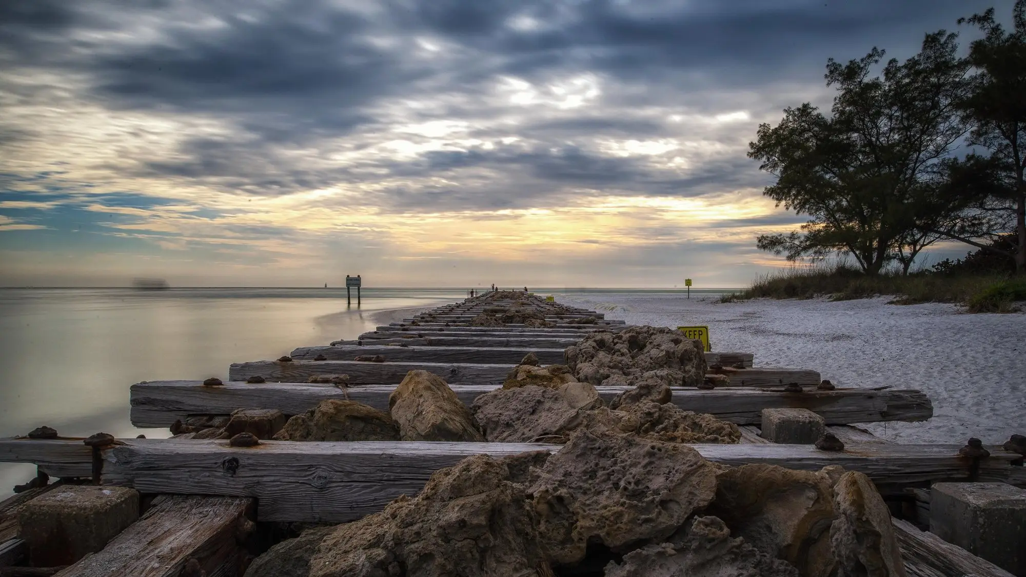 A weathered timber and rock jetty running into calm water at Longboat Pass at dusk