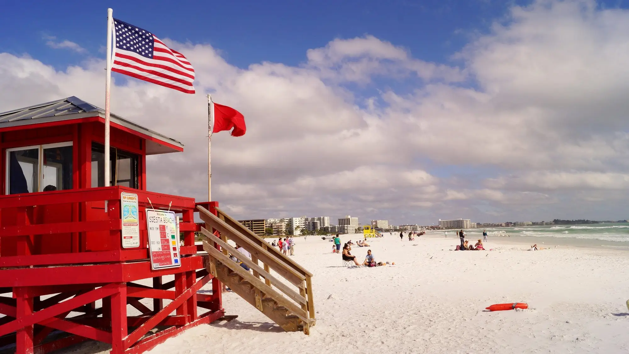 A red lifeguard stand on the white quartz sand of Siesta Beach under a blue sky