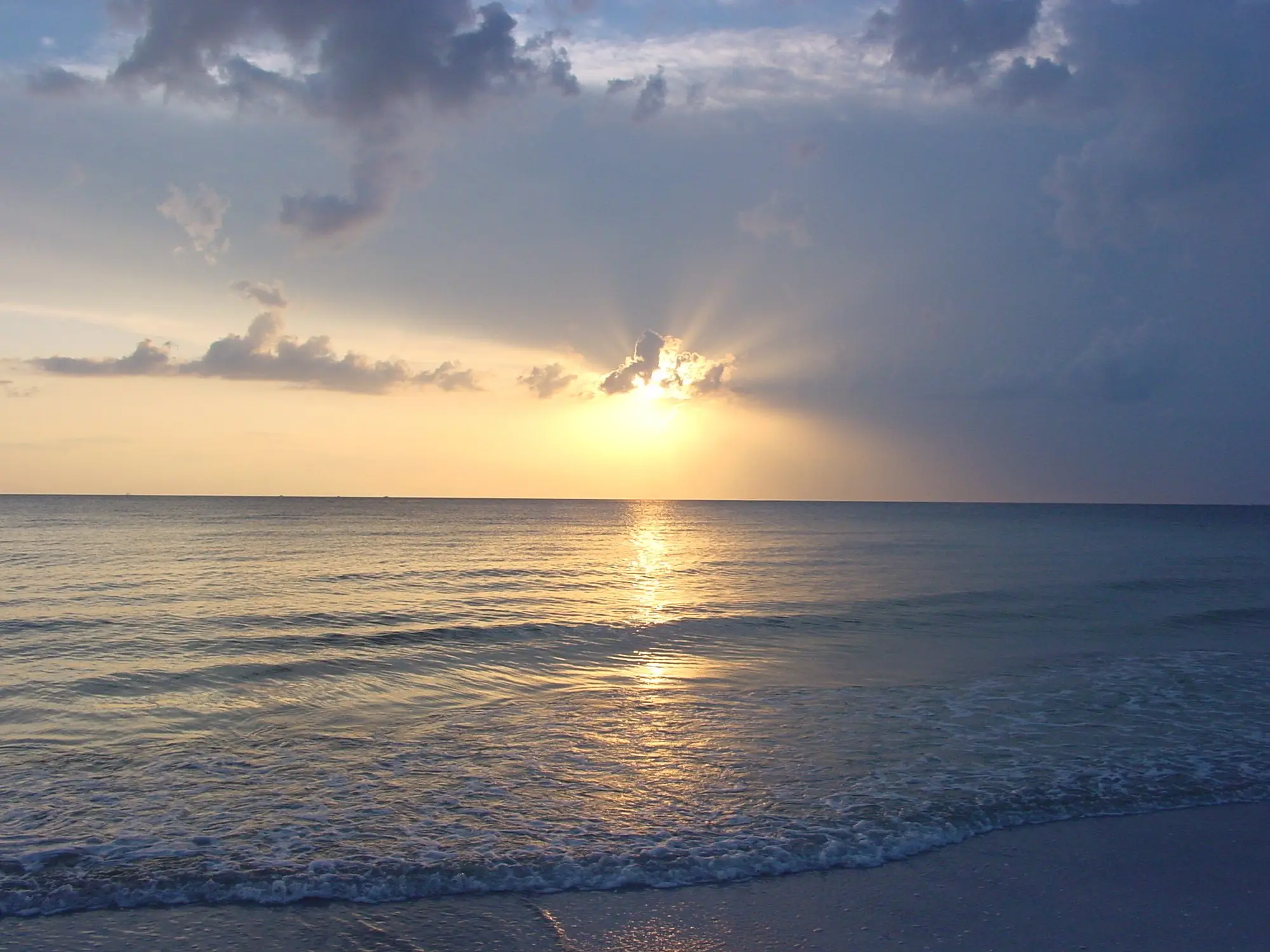 The sun breaking through clouds over calm Gulf water at North Beach in Fort De Soto Park
