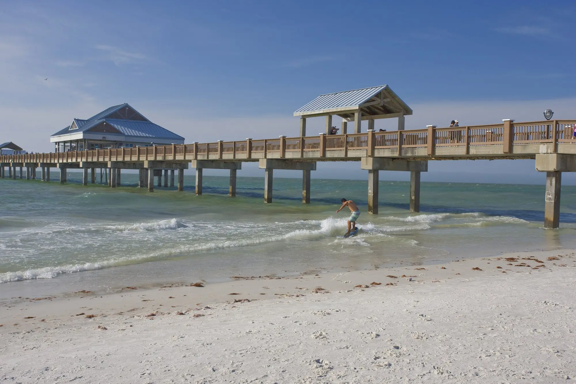 Pier 60 stretching over the surf on Clearwater Beach with white sand in the foreground