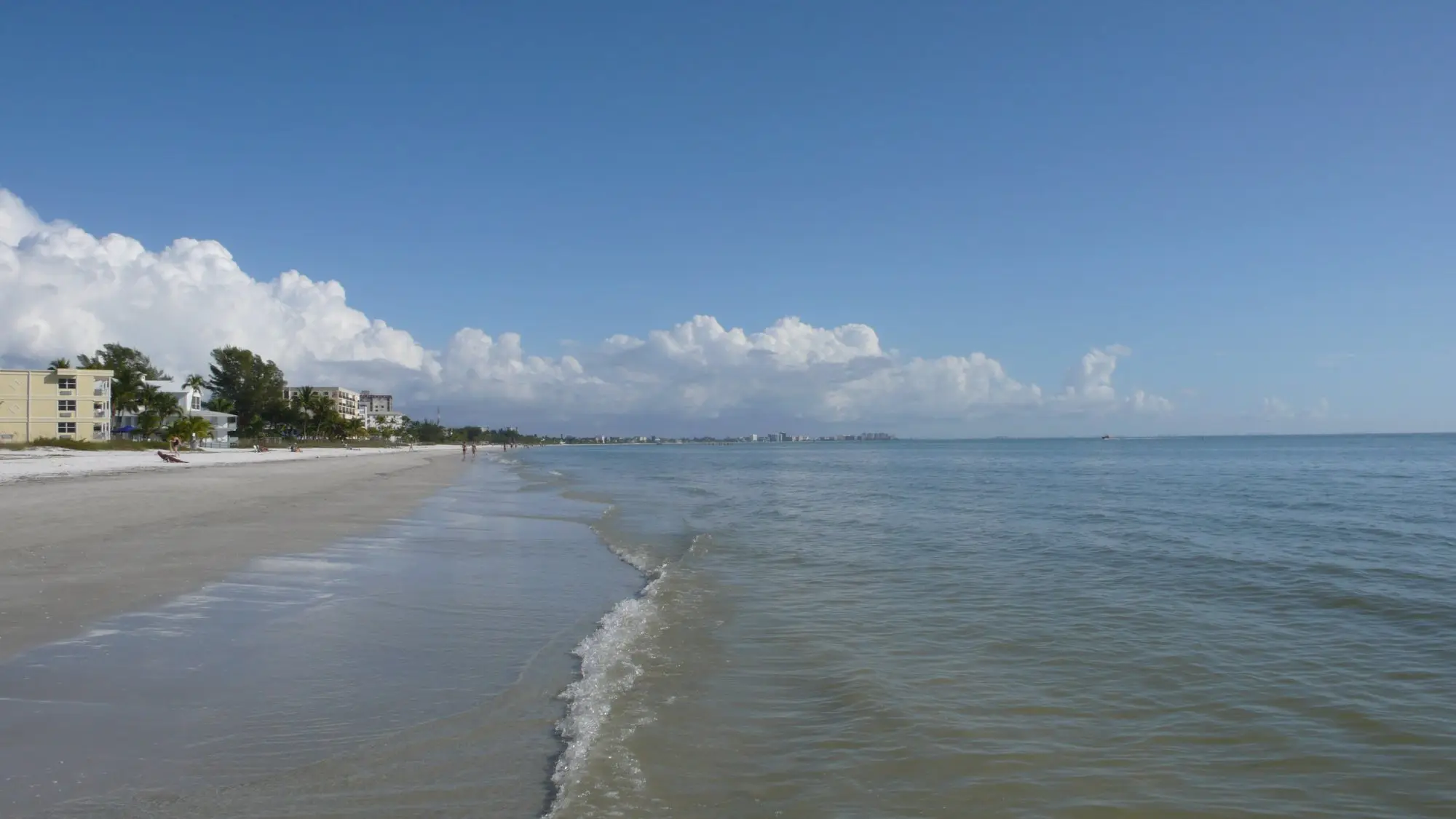 Long flat shoreline of Fort Myers Beach with gentle Gulf surf and low buildings along the sand