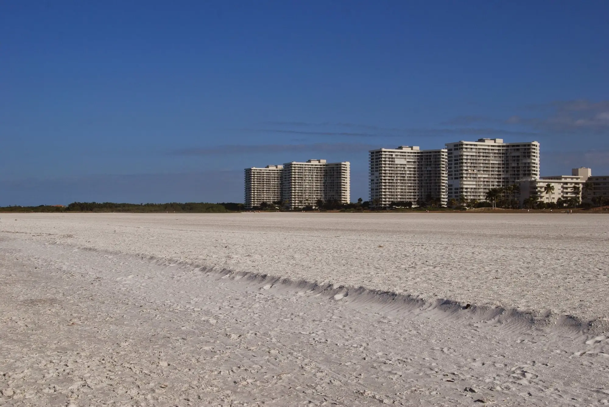Broad, empty stretch of sand on Marco Island with beachfront condo towers in the distance